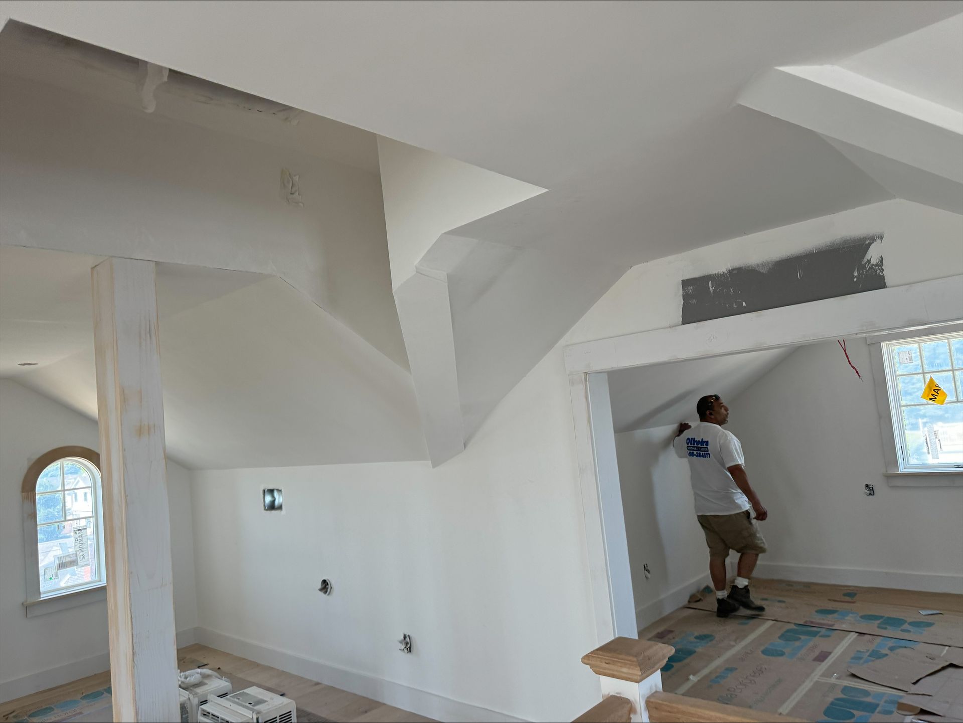 Worker painting a white room interior with covered floor and windows