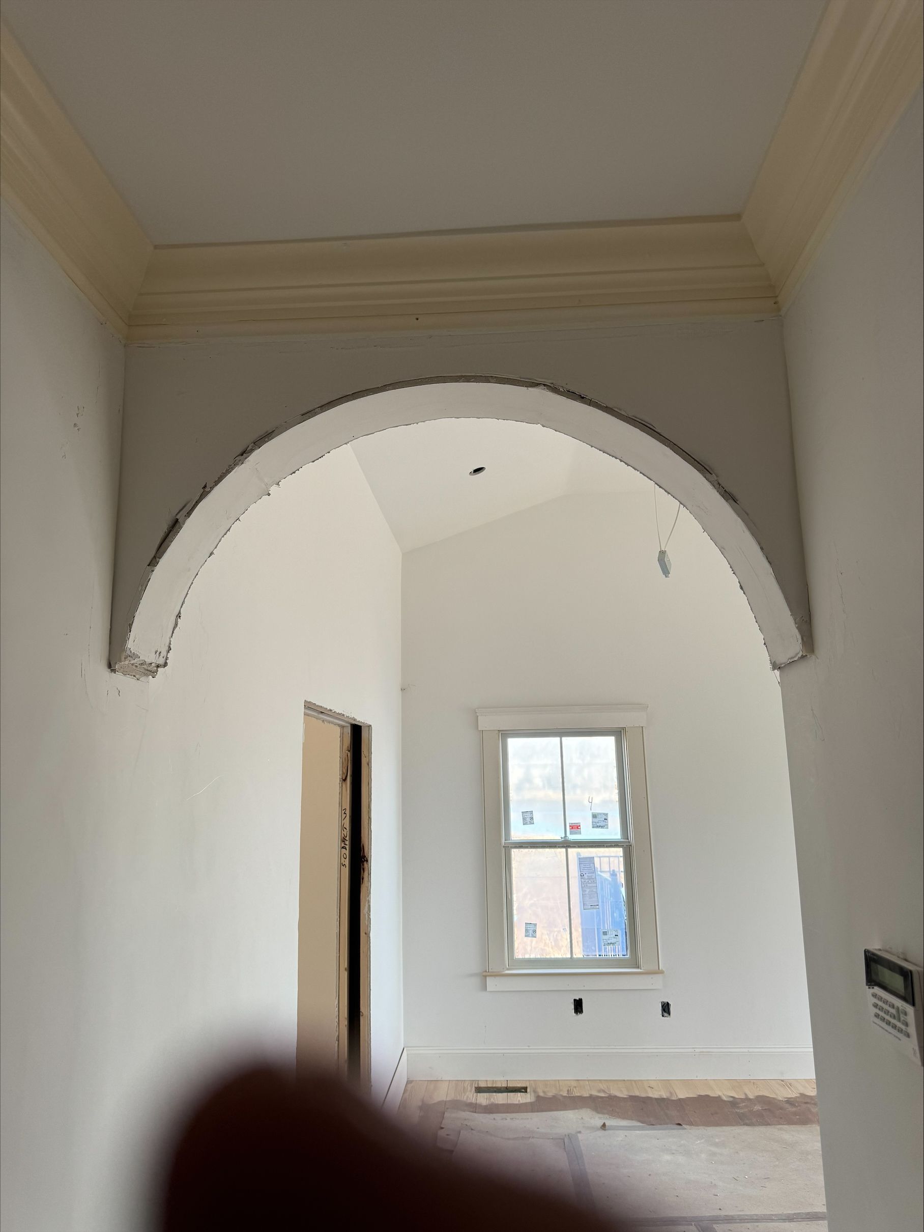 Unfinished hallway with white walls, arched opening, and a small window at the far end.
