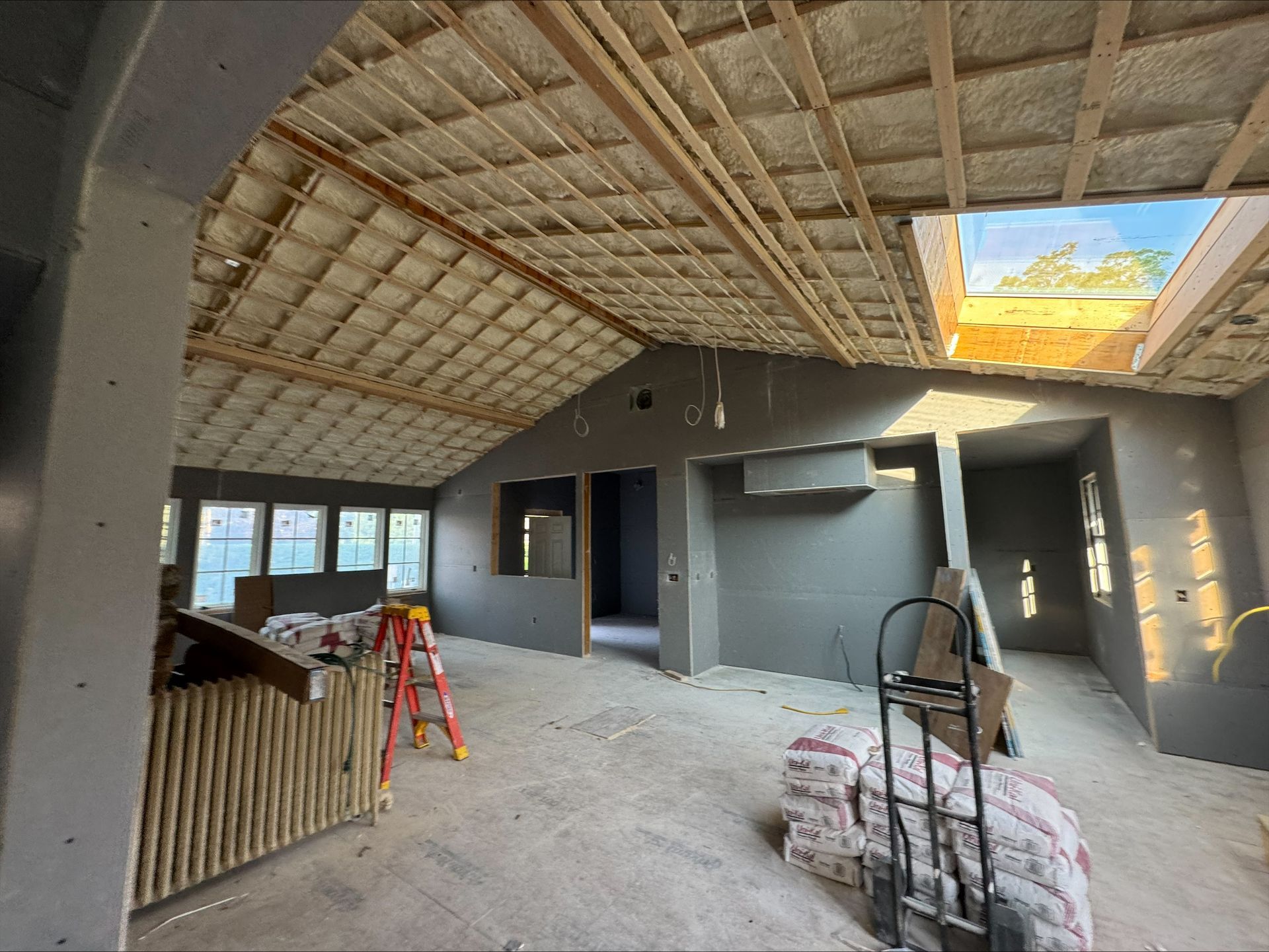 Unfinished room with exposed roof beams, gray walls, ladder, and construction materials