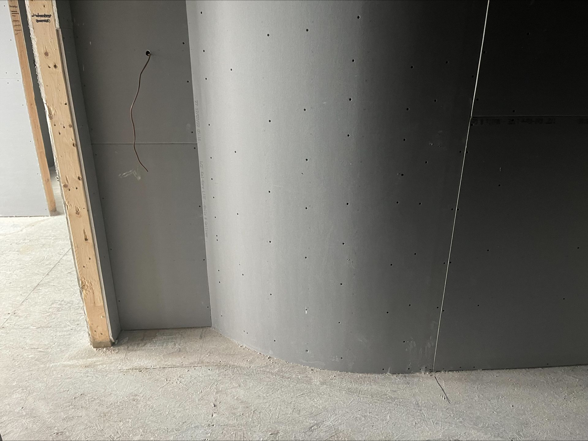 Unfinished interior wall with gray drywall corner, wooden framing, and concrete floor