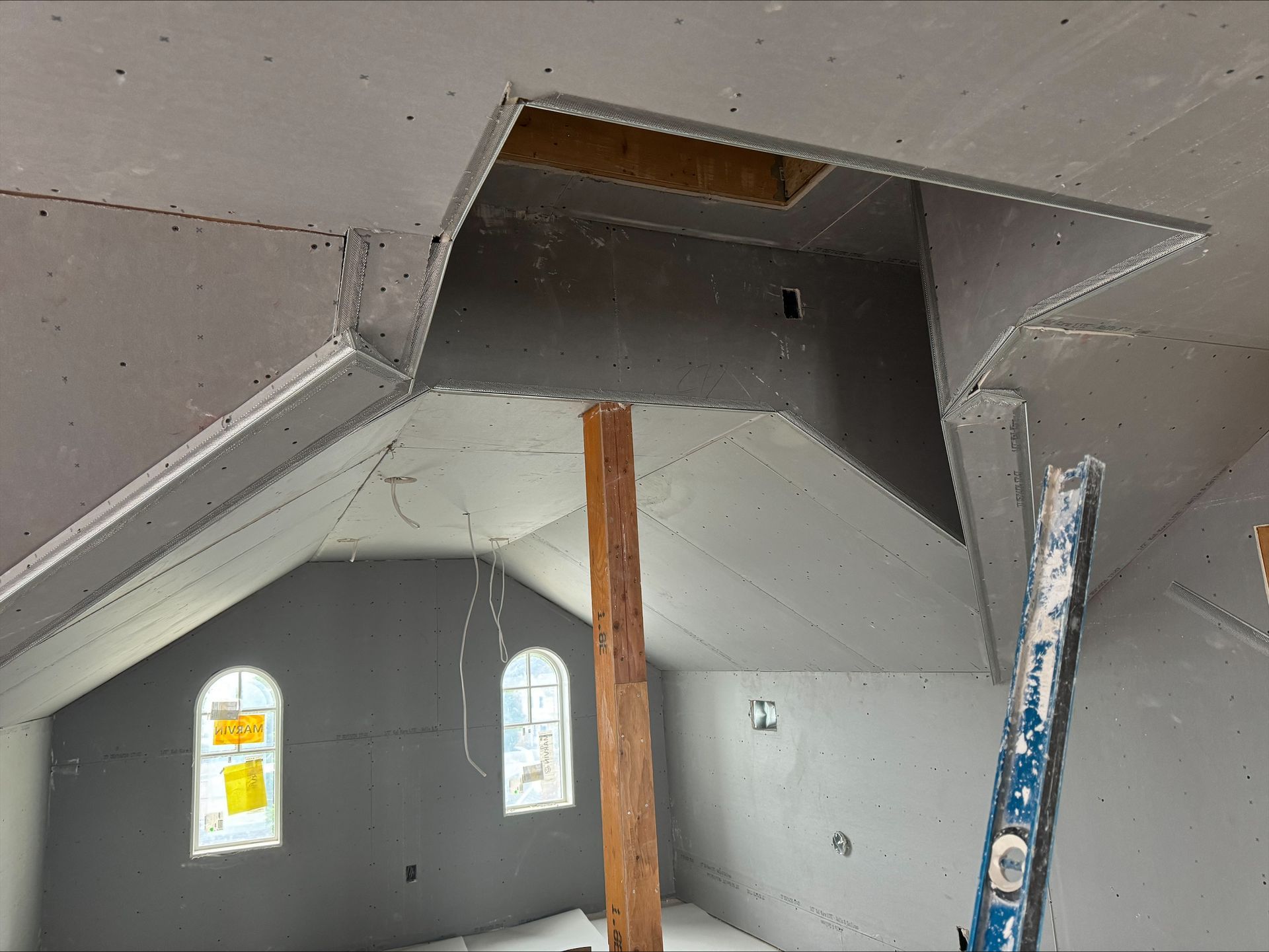 Unfinished interior with sloped drywall ceiling, open attic access, exposed beams, and two small arched windows