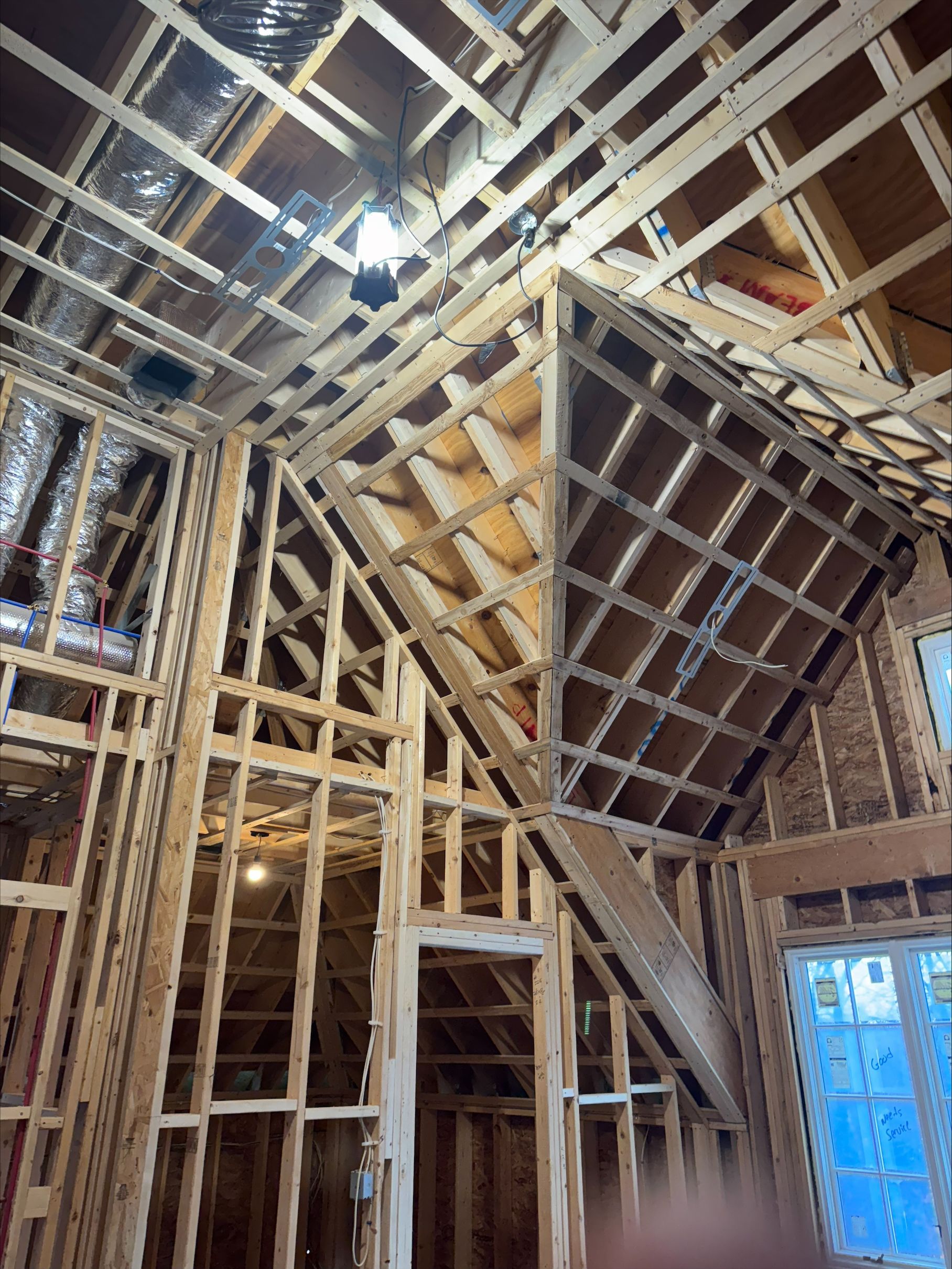 Framed house interior under construction with exposed wood studs, beams, and a sloped roof structure.