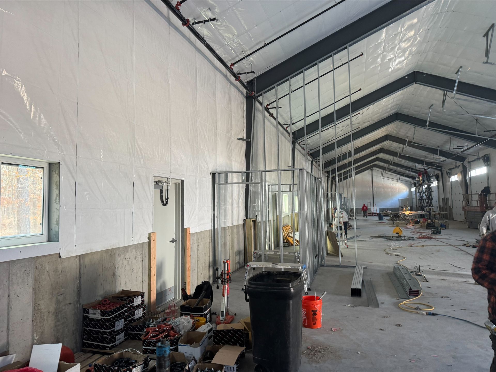 Interior of a long white tented hall with construction materials, trash bins, and a few workers in the distance