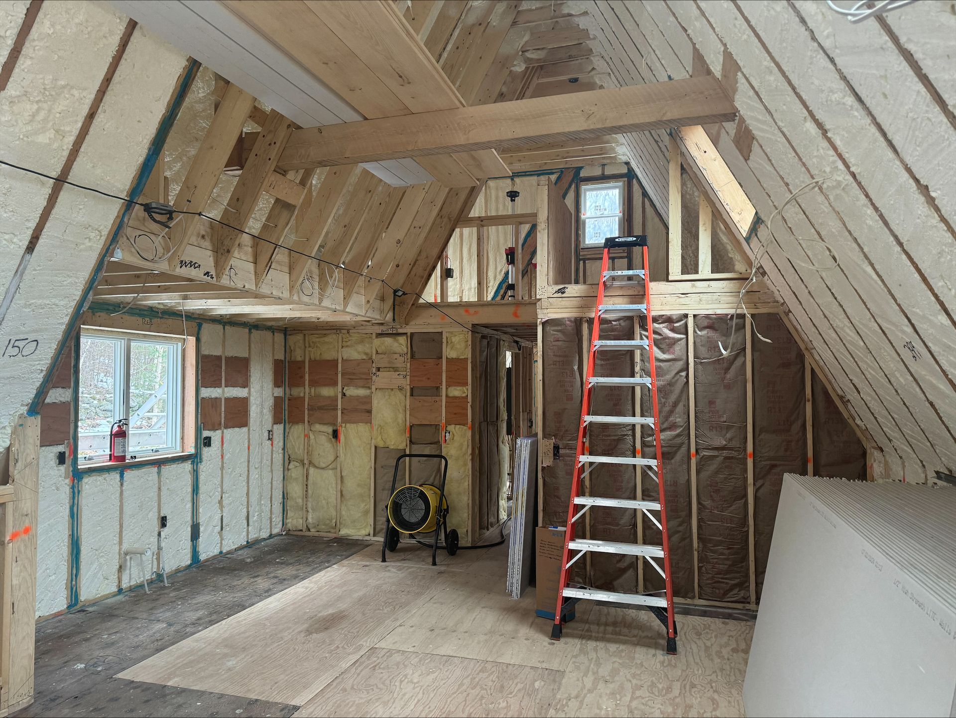 Unfinished attic with exposed wooden beams, ladder, insulation, and construction tools under renovation