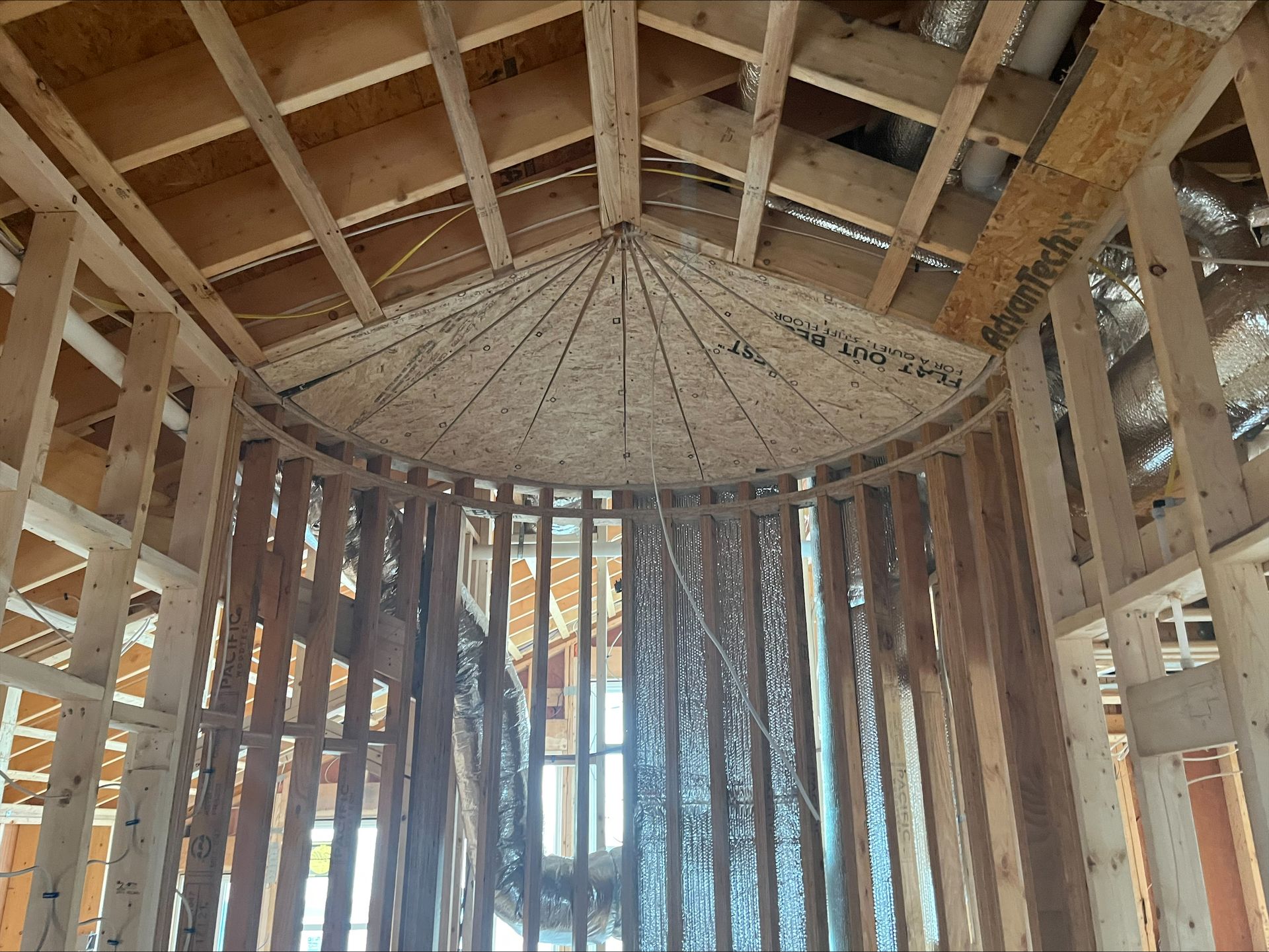 Interior of a wooden-framed structure under construction, showing roof rafters and vertical studs.