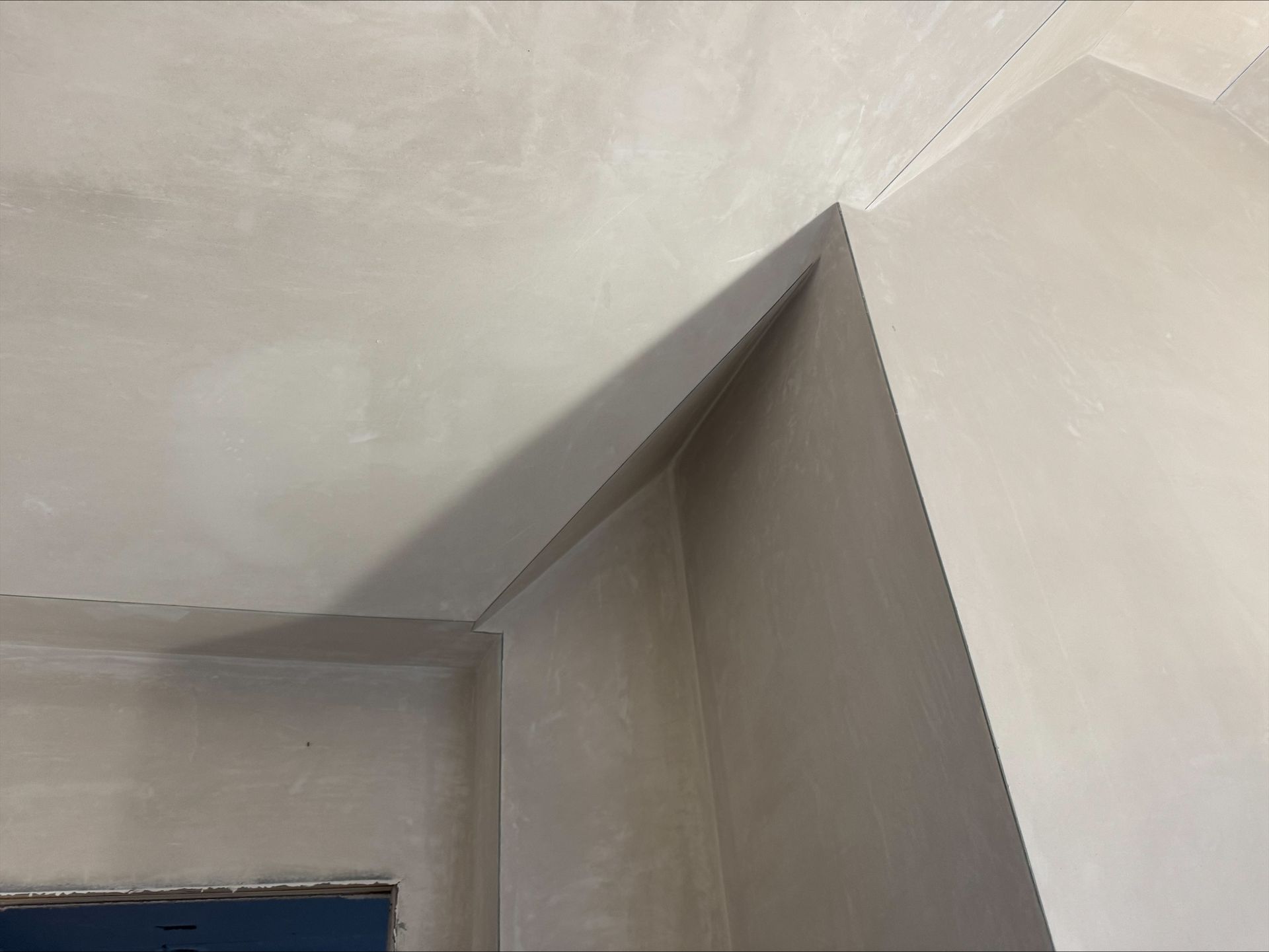 Corner of a room with gray walls and ceiling, showing a sharp angled ceiling seam above a doorway.