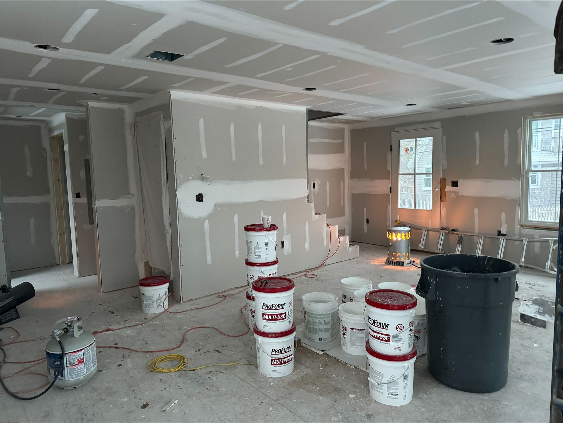 Partially finished room with drywall, paint buckets, and construction tools on the floor