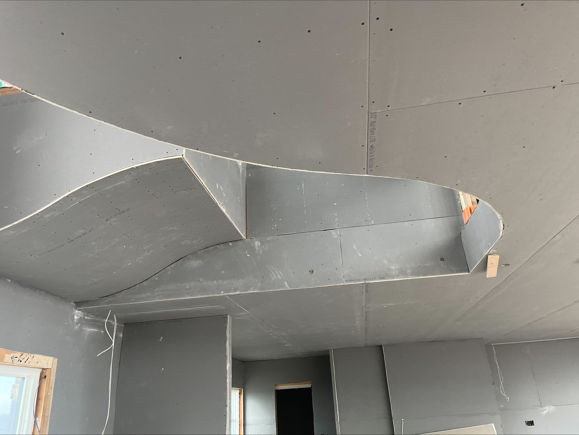Gray unfinished ceiling with exposed drywall and a curved soffit in an interior room