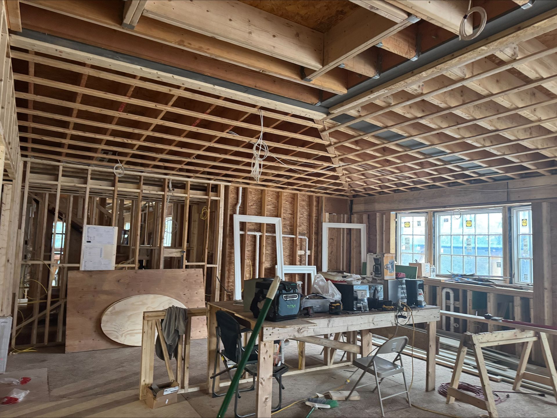 Exposed-framing interior under construction with scaffolding, tools, and daylight through windows