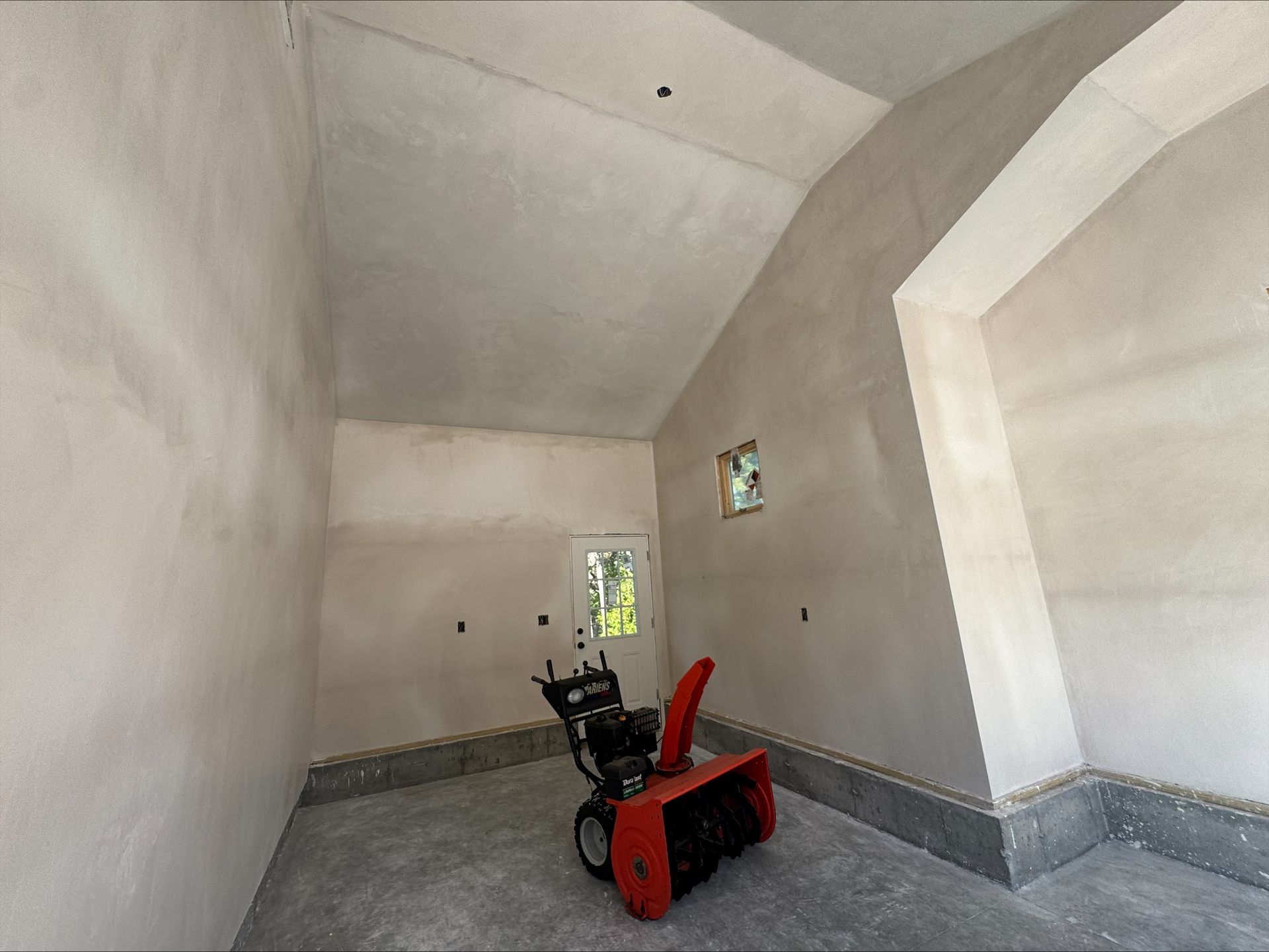 Empty room with a red and black snowblower on a concrete floor