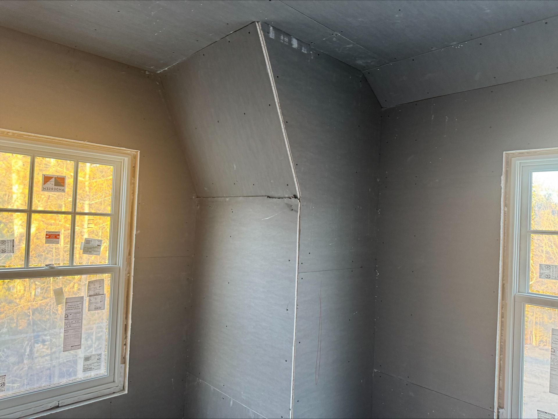 Room interior with gray drywall and two windows letting in warm sunlight