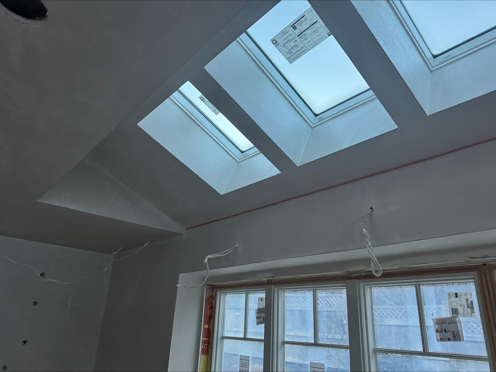Slanted ceiling with three skylight windows above a room window and light gray walls