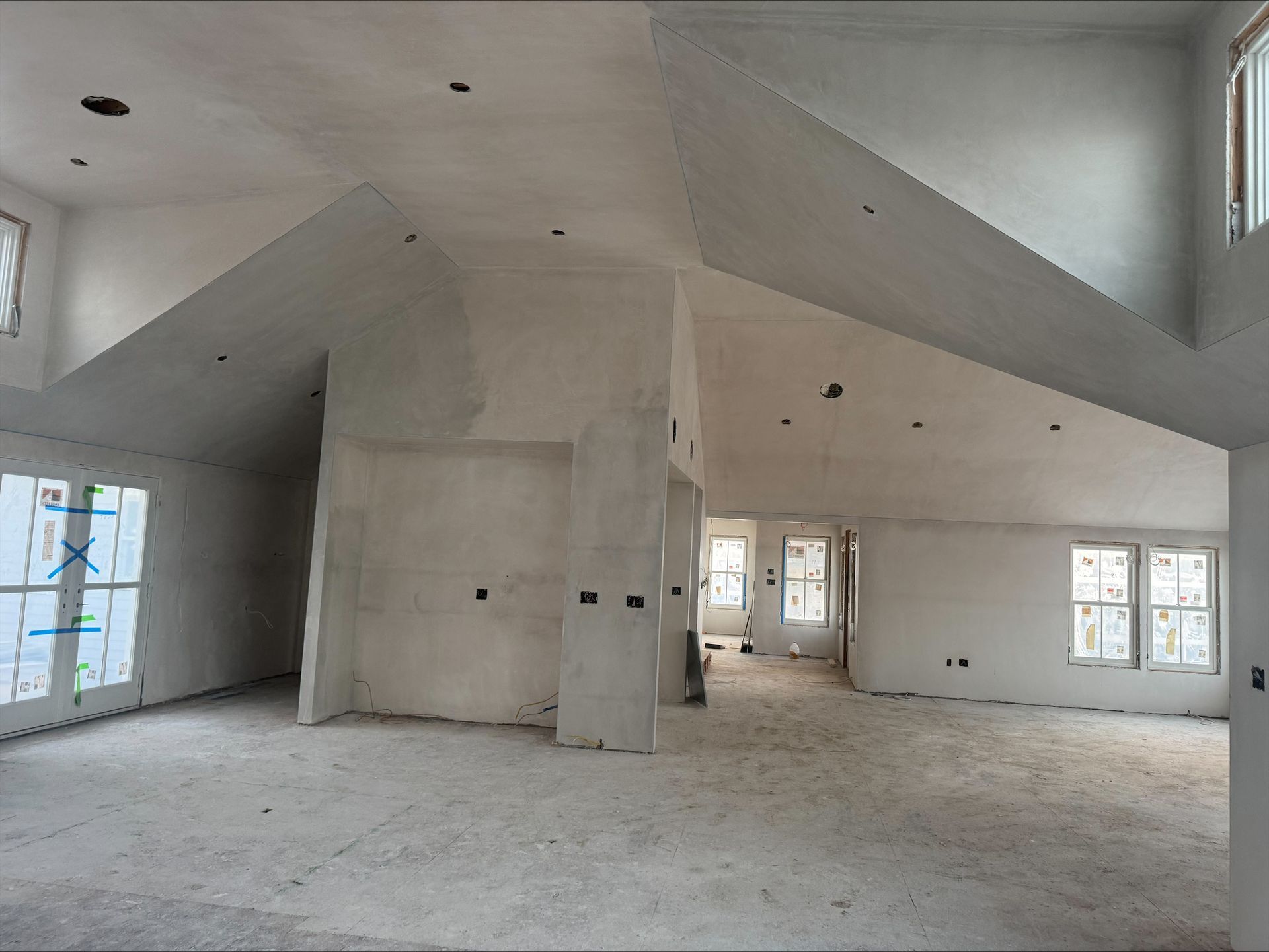 Empty unfinished room with exposed drywall, high sloped ceilings, and windows letting in natural light