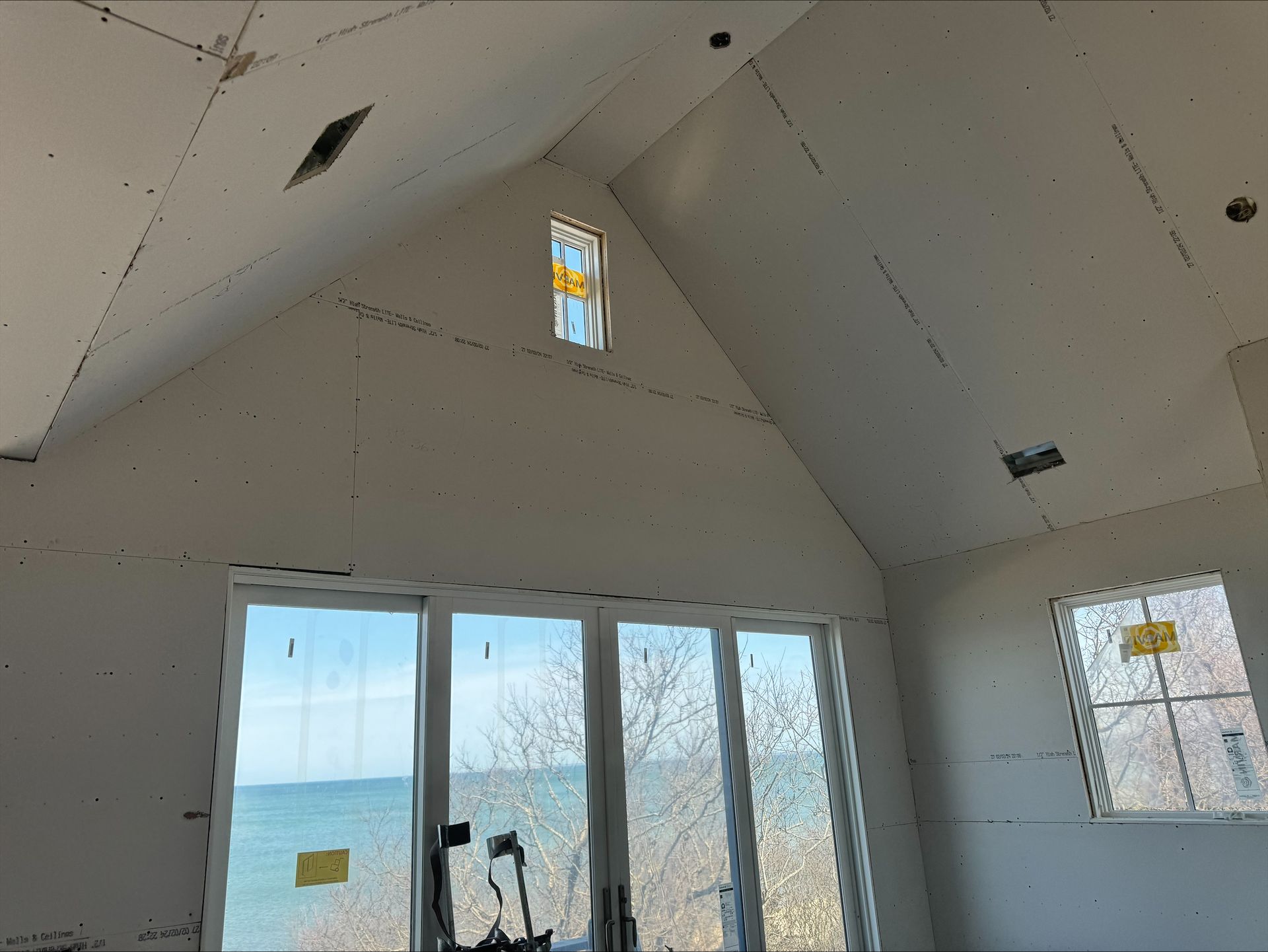 Unfinished room with sloped white walls, large windows, and a view of trees and sky.