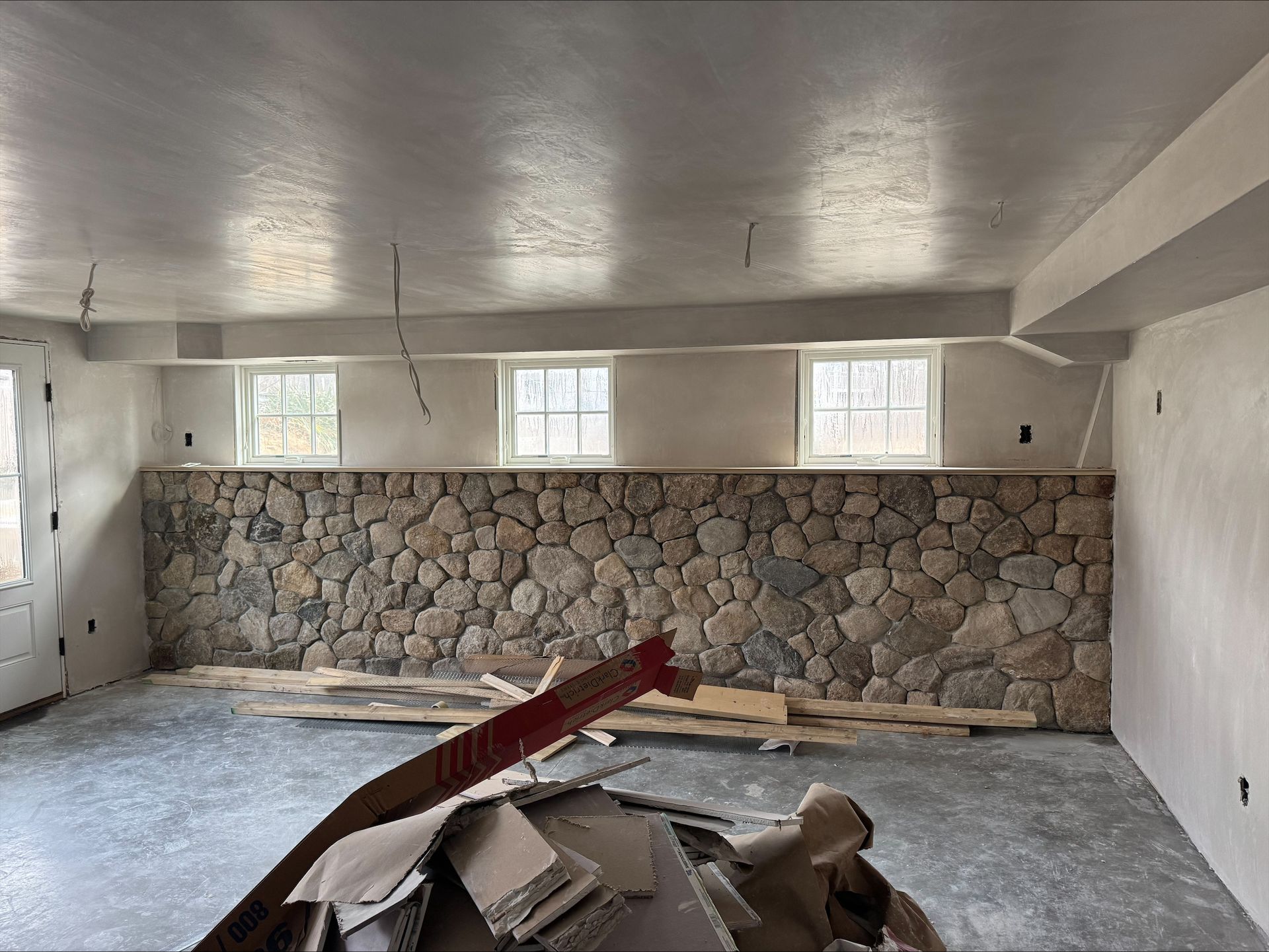 Renovation room with stone accent wall, small windows, and construction debris on the floor