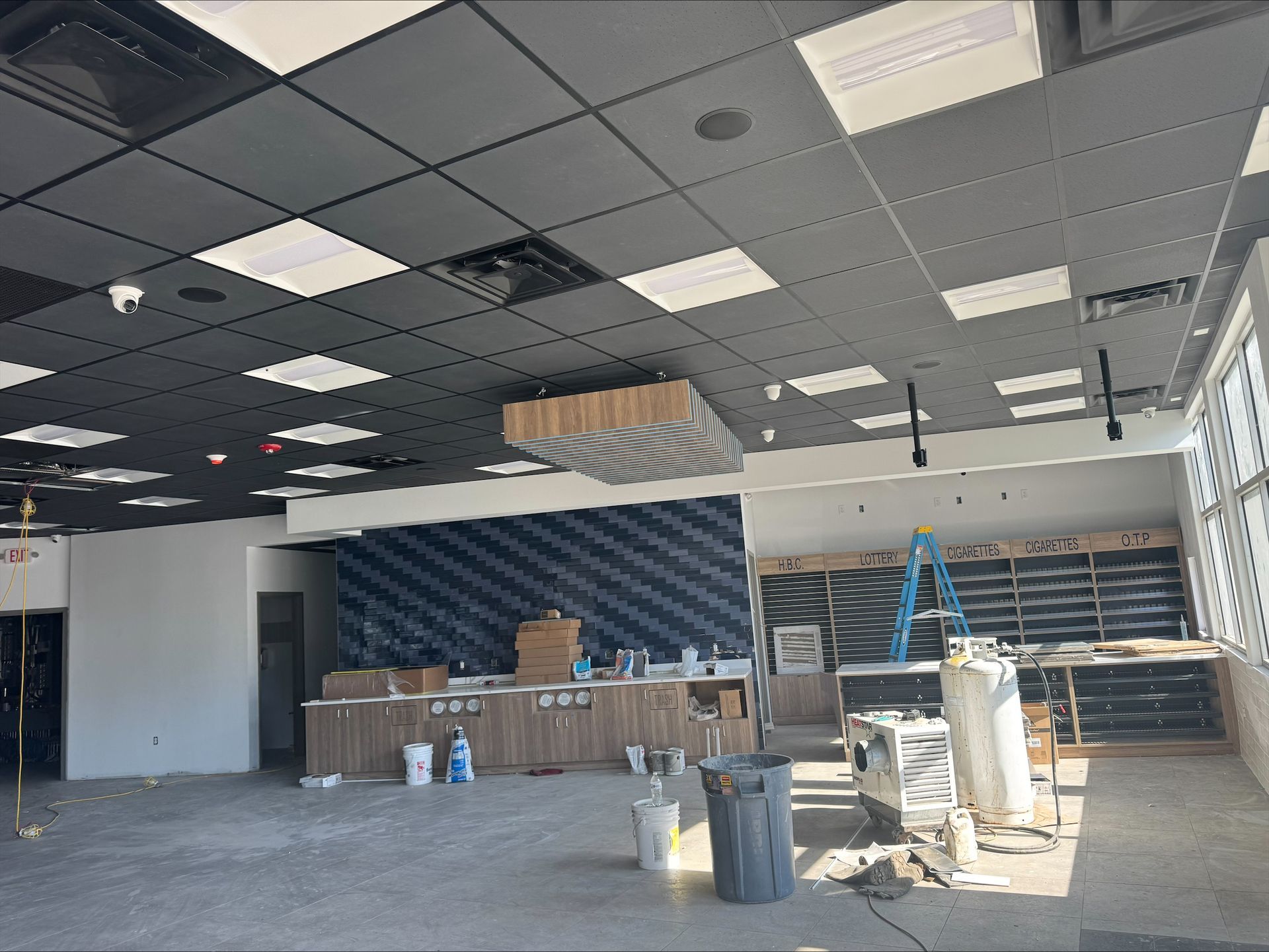 Empty office under renovation with exposed ceiling tiles, drywall, tools, and stacked materials