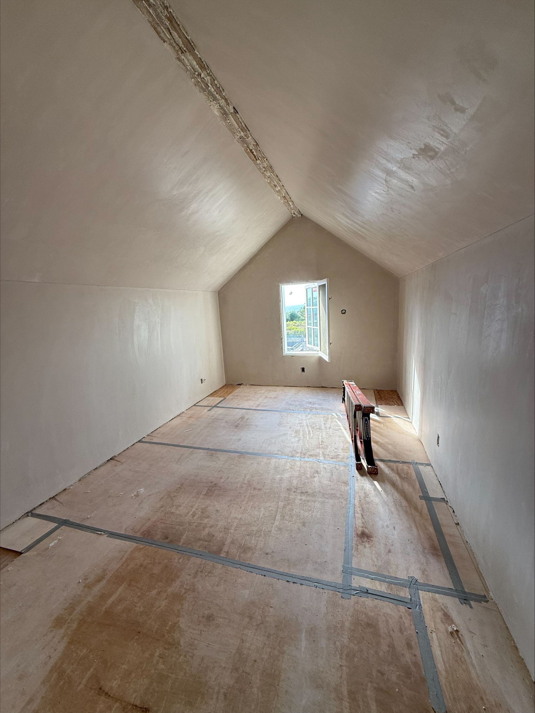 Narrow white attic room with a small window and a cat walking on the floorboards