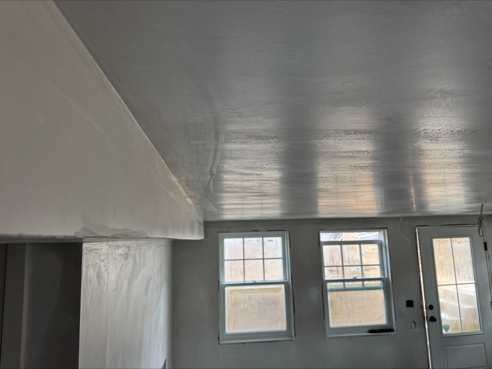 Small unfinished room with white walls, gray ceiling, three windows, and a door with light blue trim.