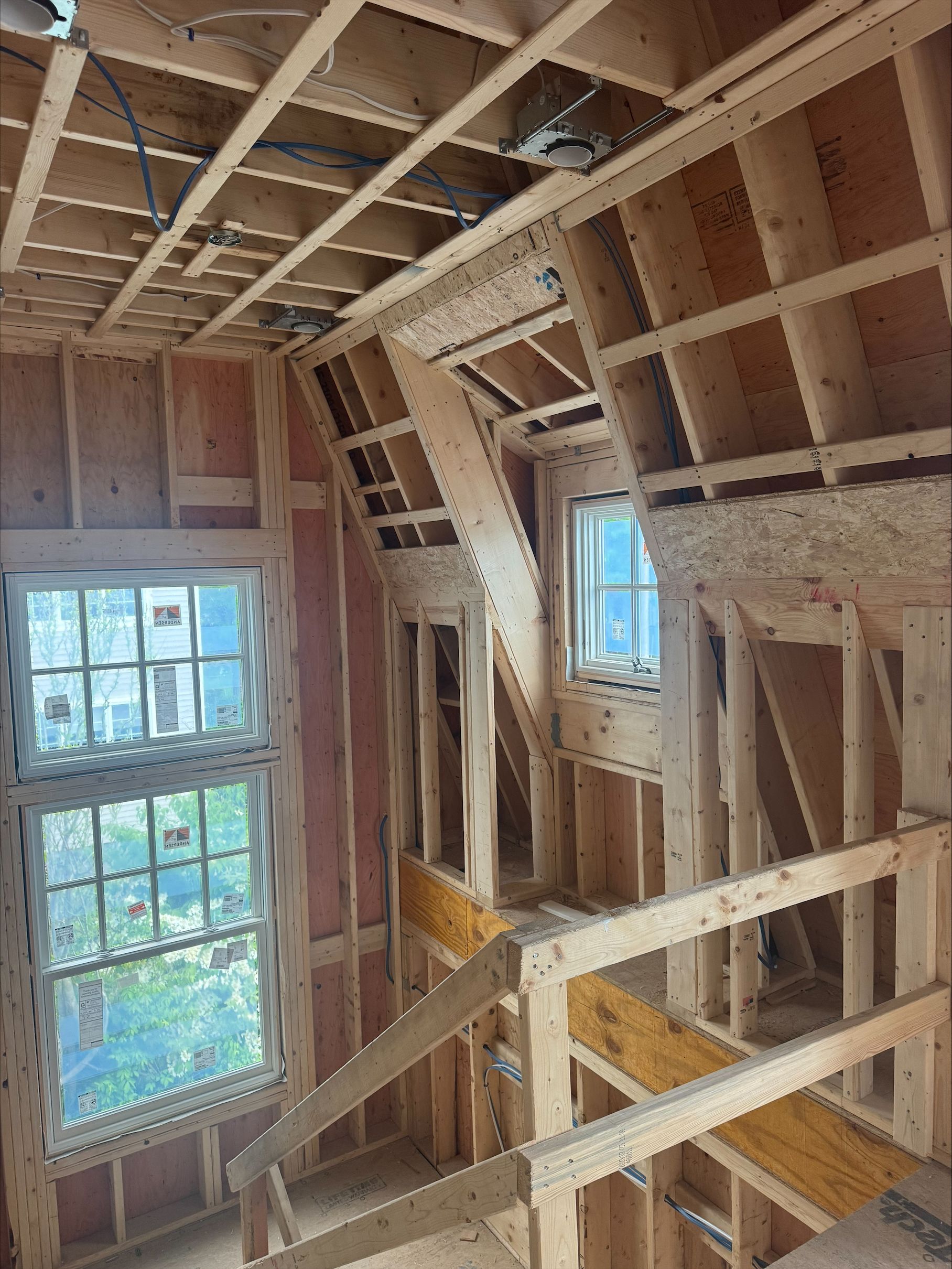 Interior of a house under construction with exposed wooden framing and two windows showing daylight.