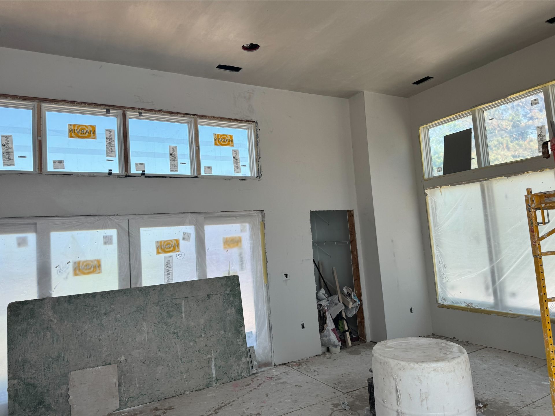 Unfinished room with exposed drywall, windows, construction materials, and a scaffold.