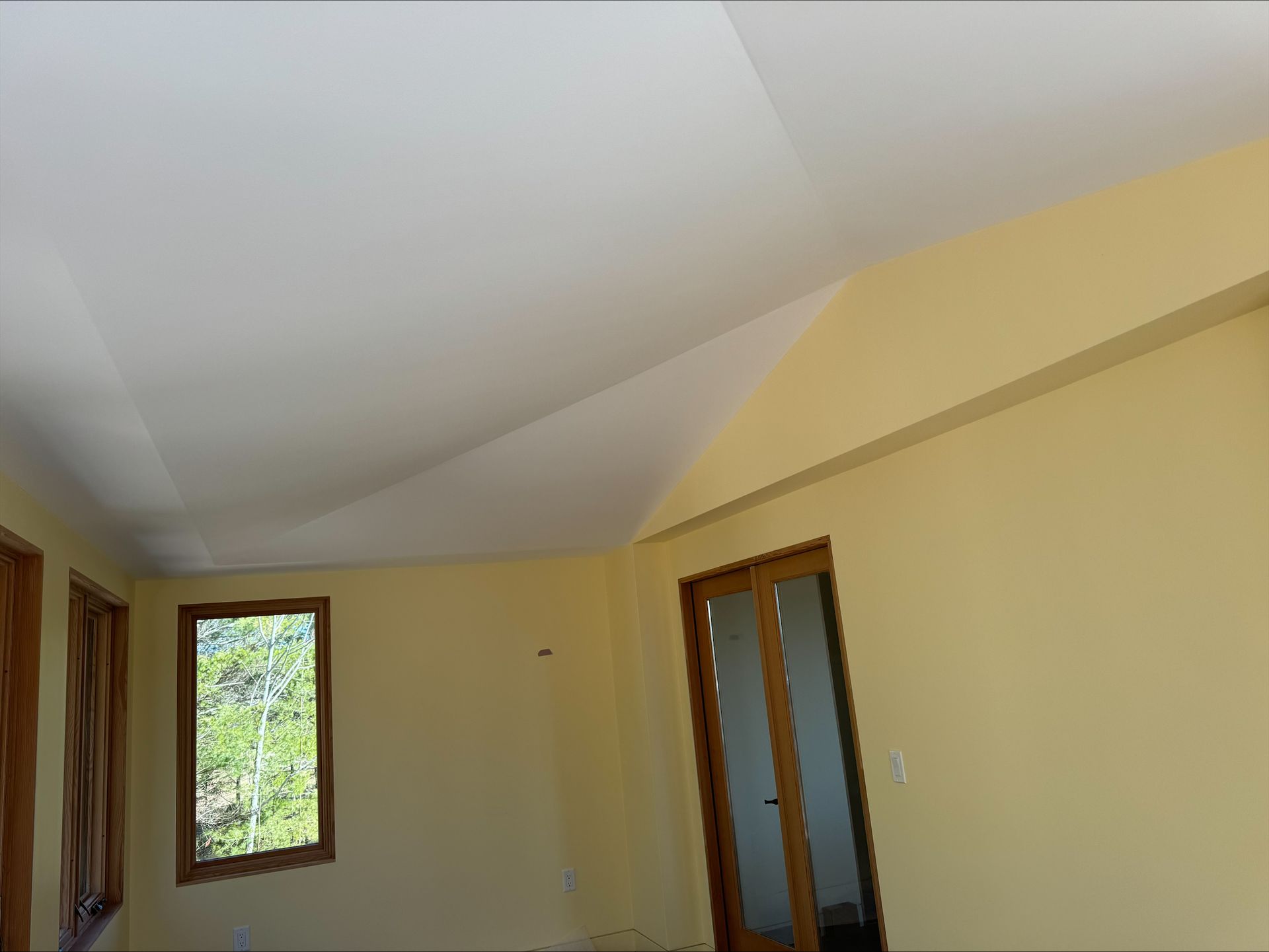 Empty yellow room with a window, door, and white ceiling.