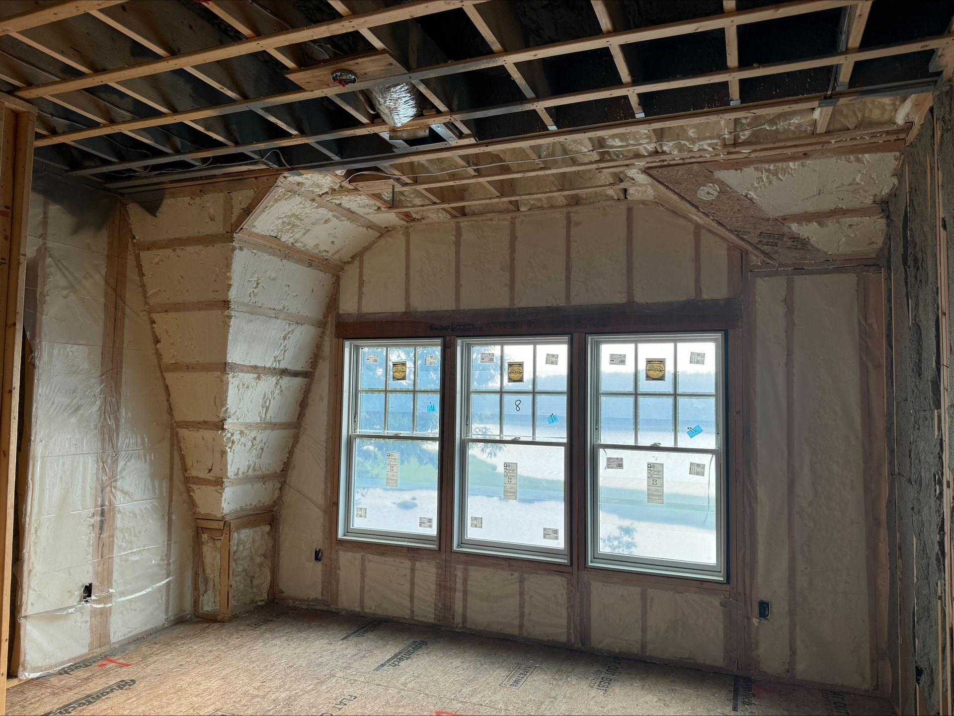 Partially renovated room with exposed ceiling joists, unfinished walls, and a large window letting in light