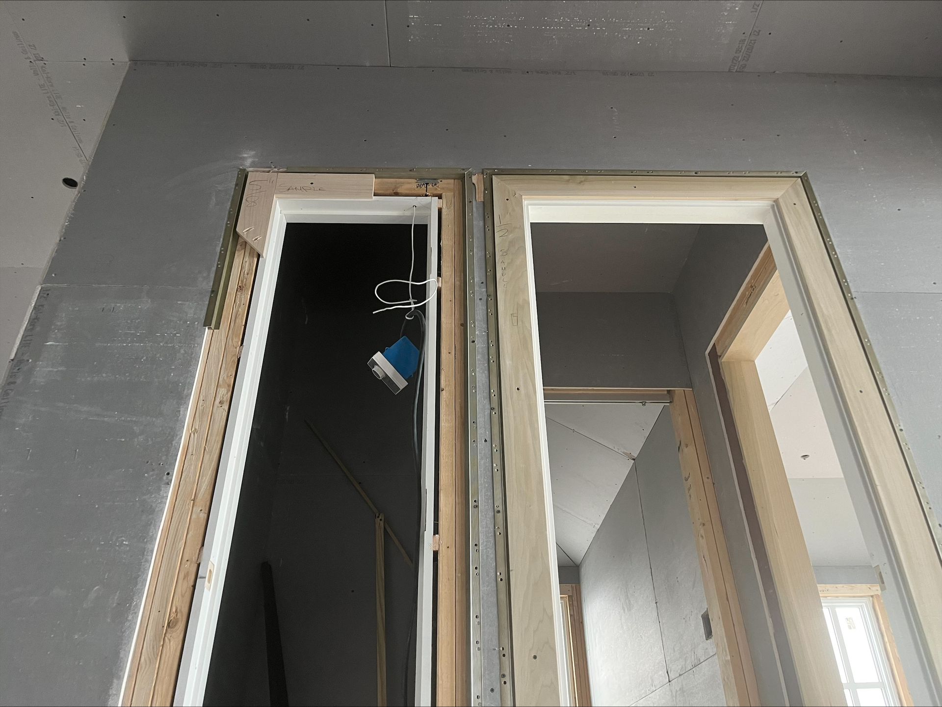 Open doorway to a closet under construction with exposed framing and hanging blue electrical wire.