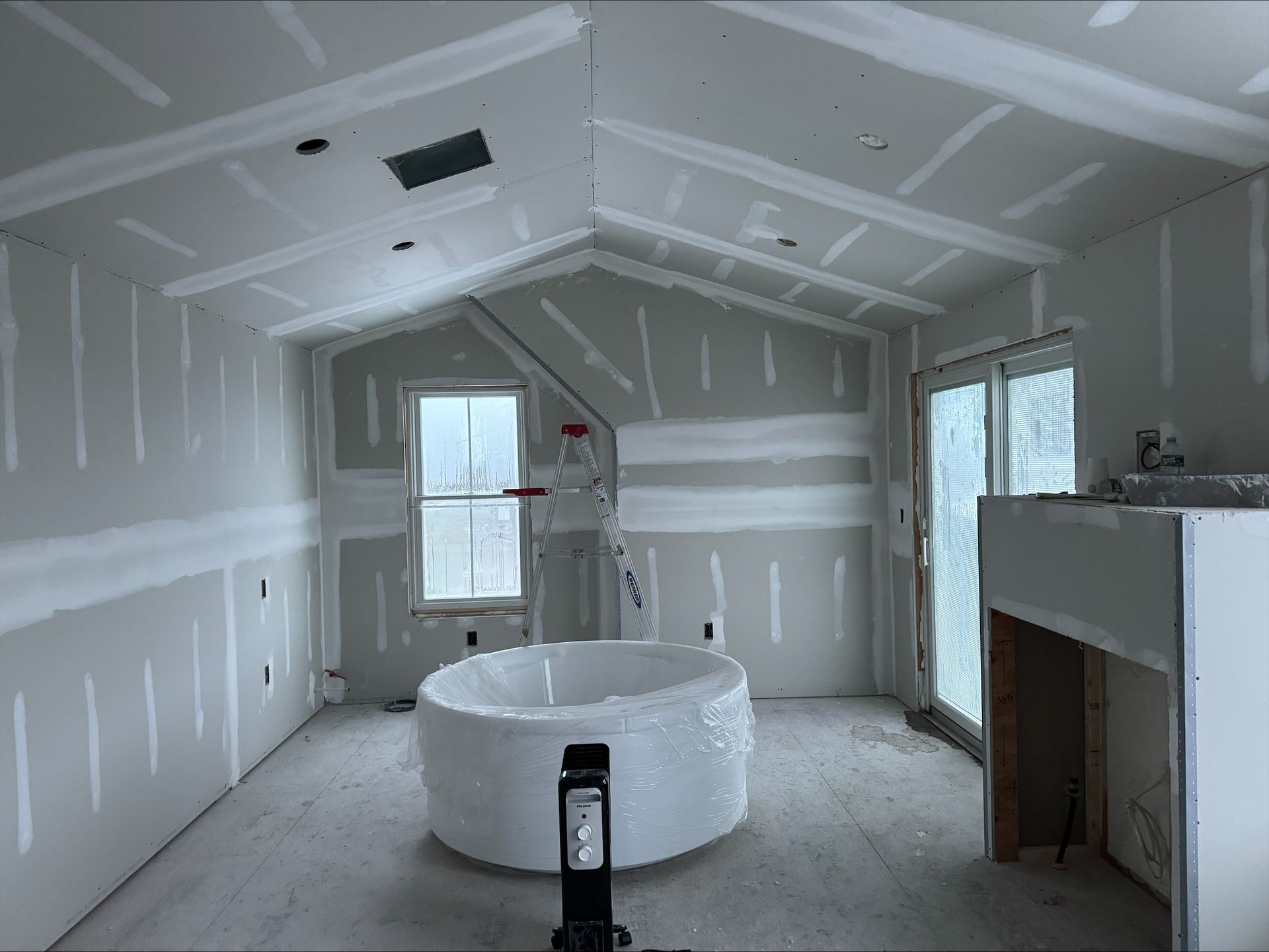 Unfinished room with drywall, a white bathtub in the center, and a windowed wall.