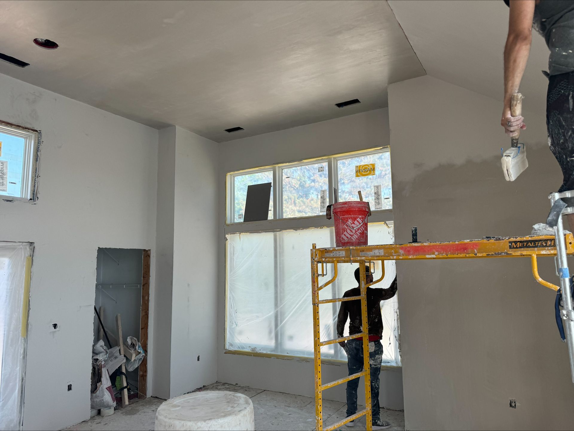 Partially painted room with workers on a scaffold and ladder during interior renovation