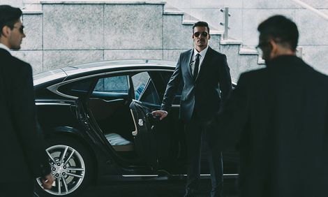 A man in a suit and tie is standing next to a car.