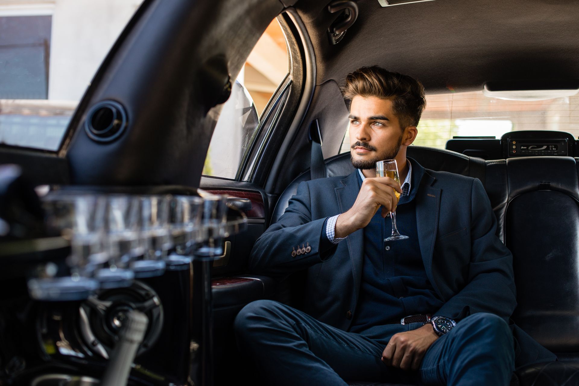 A man in a suit is sitting in the back seat of a limousine holding a glass of wine.
