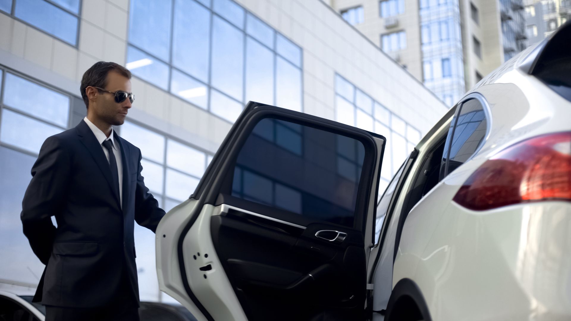 A man in a suit and tie is opening the door of a car.