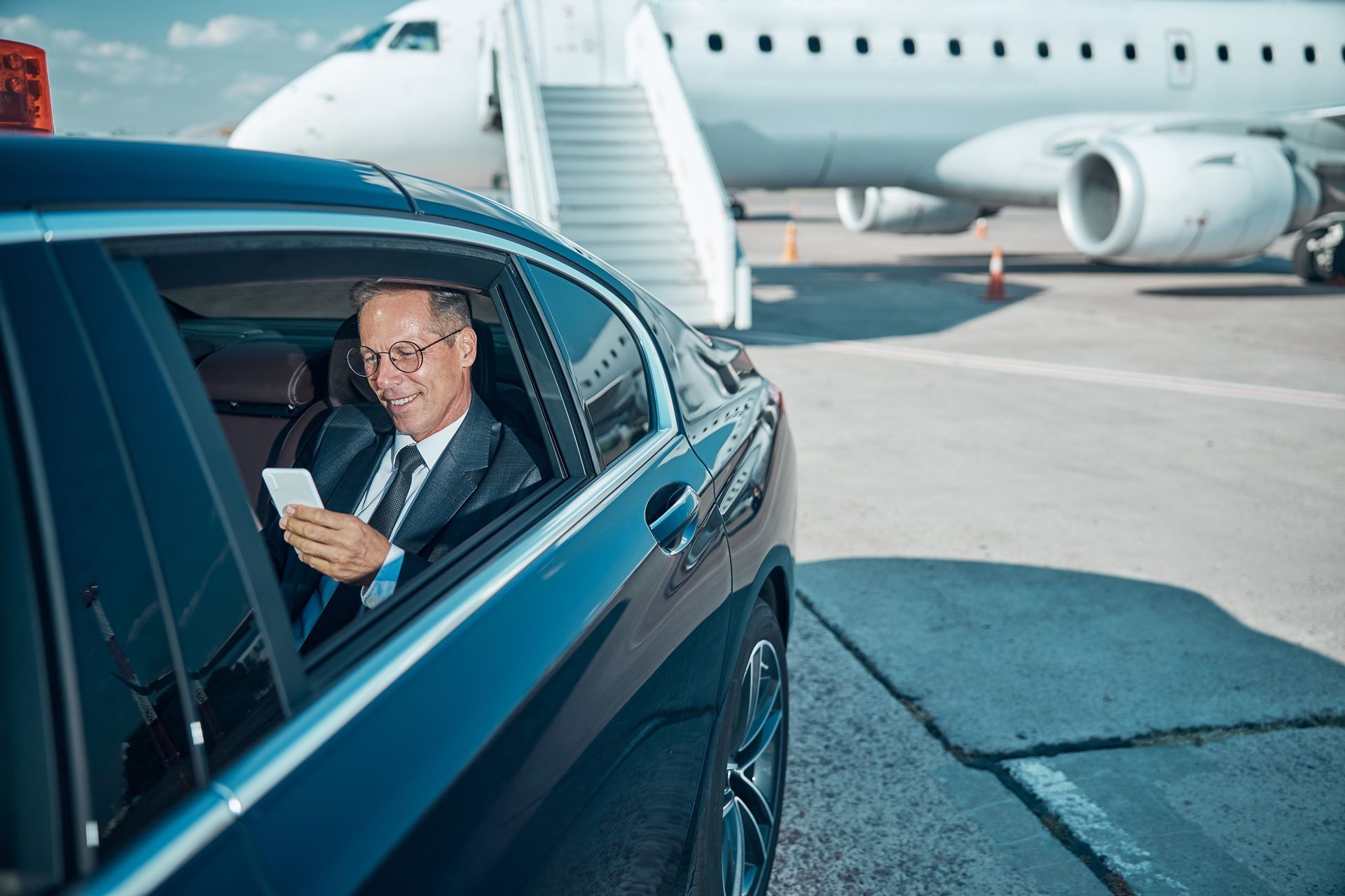 A man is sitting in a car looking out the window at an airplane. A man is sitting in a car looking out the window at an airplane.