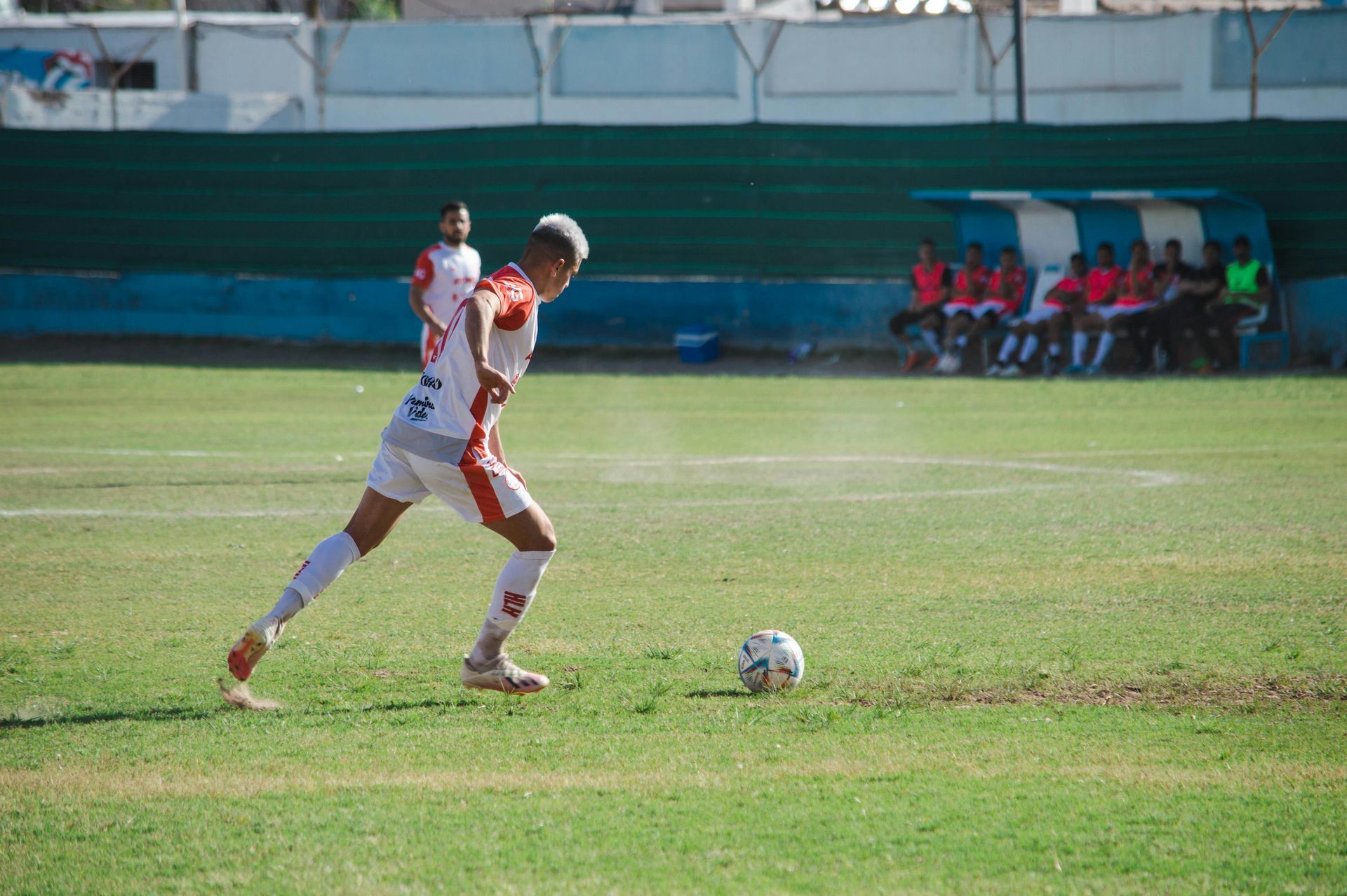 Soccer player in white and orange uniform about to kick the ball on a green field.