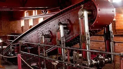 Large, red beam engine with silver pipes in a brick building.
