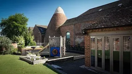 Brick building with an oast house, playground, and glass doors on a sunny day.