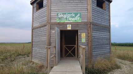 Wooden Skylark Tower with open door, overlooking a field.