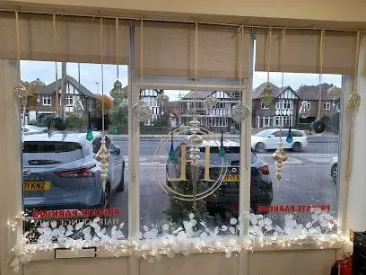 Shopfront window decorated with lights and ornaments, view of cars and houses outside.