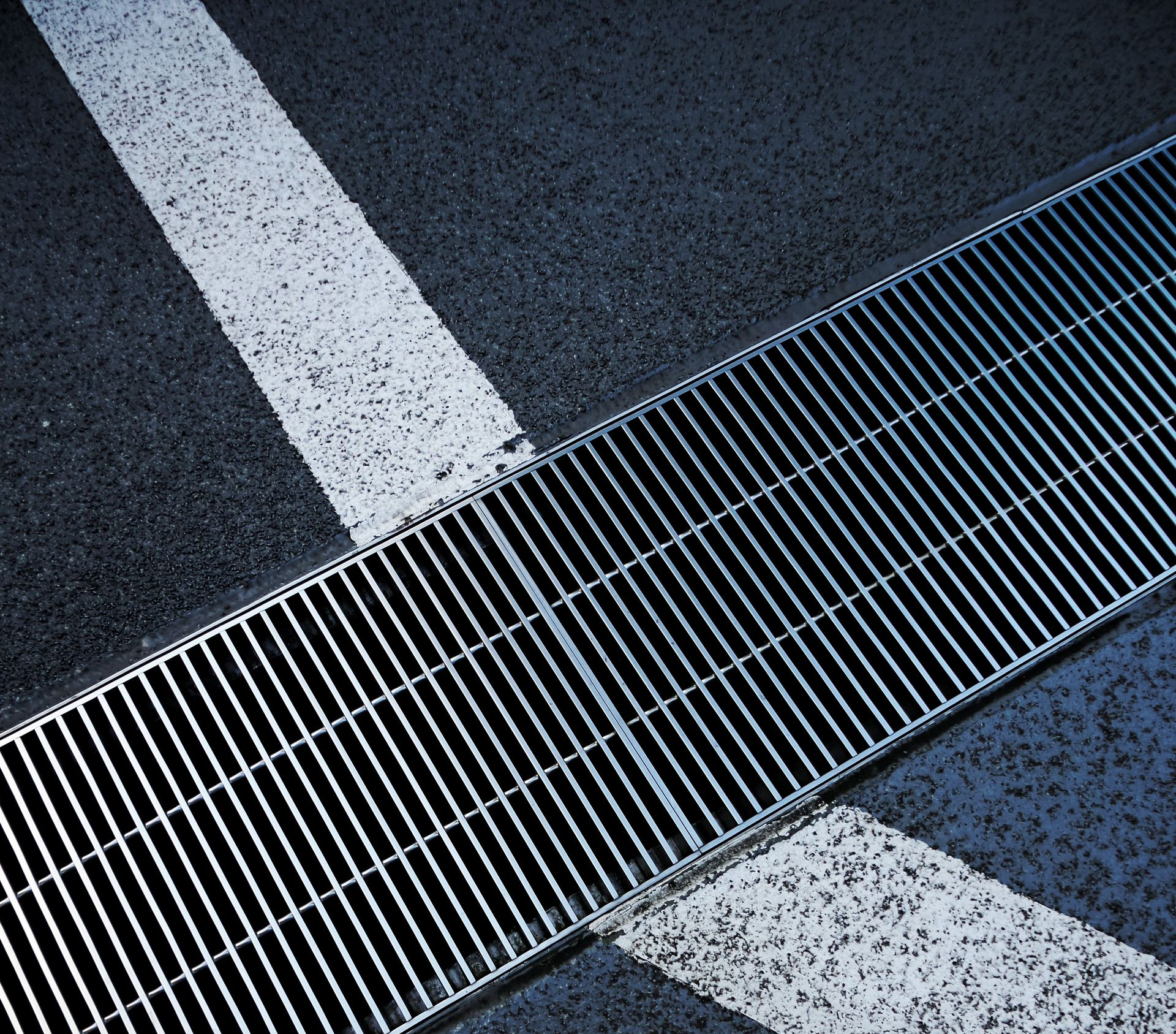 Close-up of asphalt with a white lane stripe and a metal drainage grate crossing the pavement.