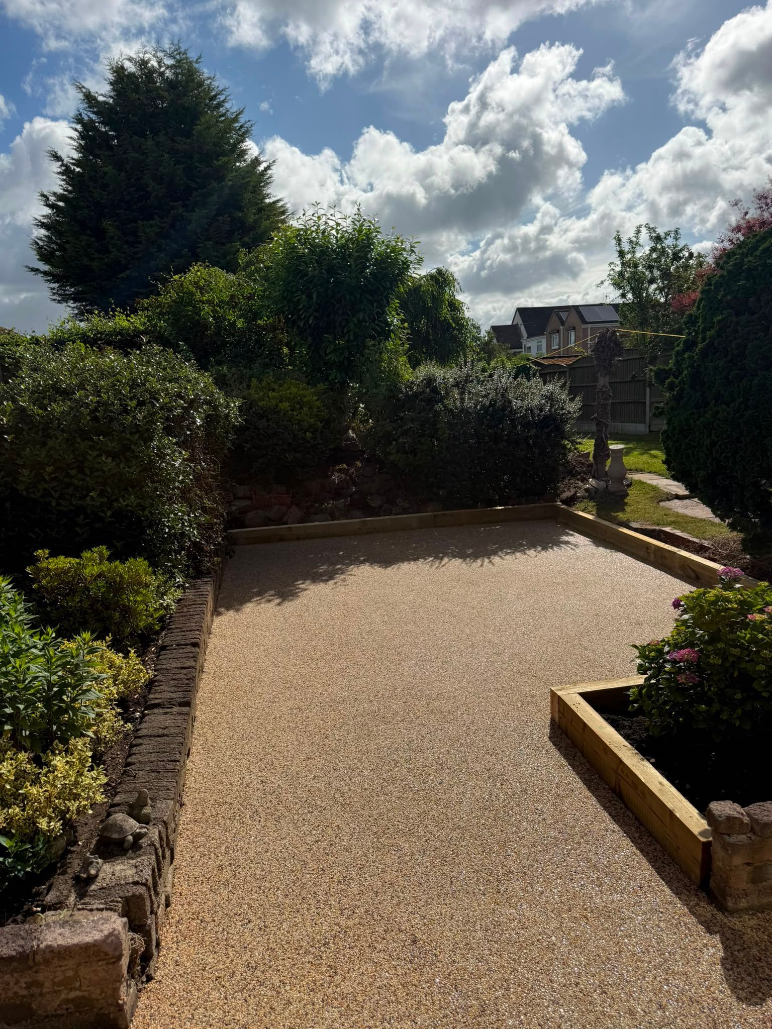 Gravel garden path bordered by shrubs and flowers under a partly cloudy sky
