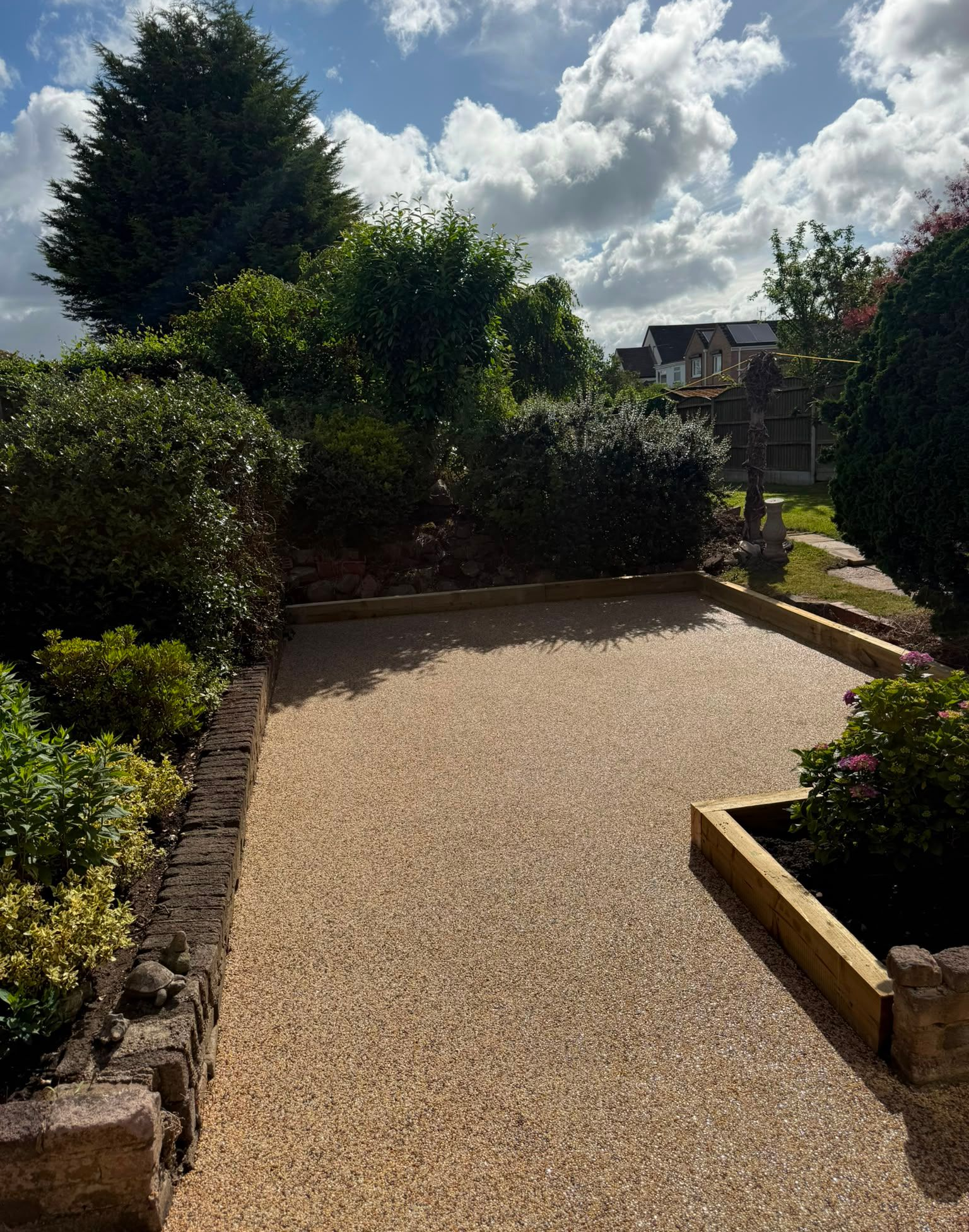 Gravel garden path bordered by stone planters and shrubs under a bright, cloudy sky