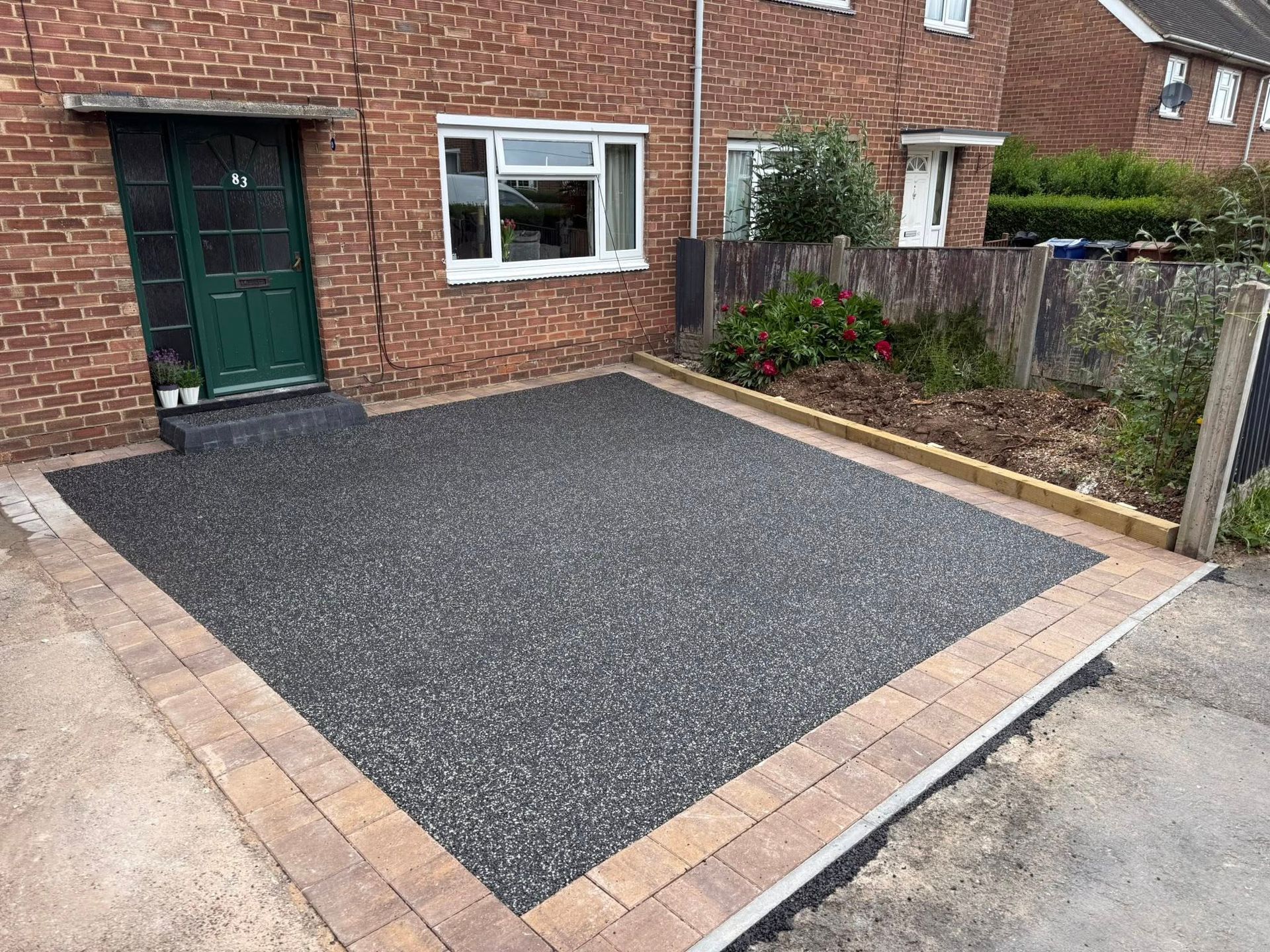 Brick house front yard with a newly paved dark gravel driveway bordered by tan pavers
