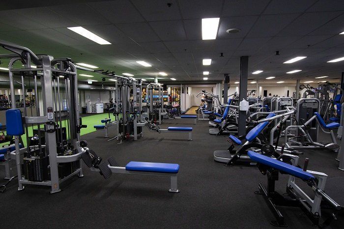 Empty gym with weight machines, benches, and cardio equipment under bright ceiling lights