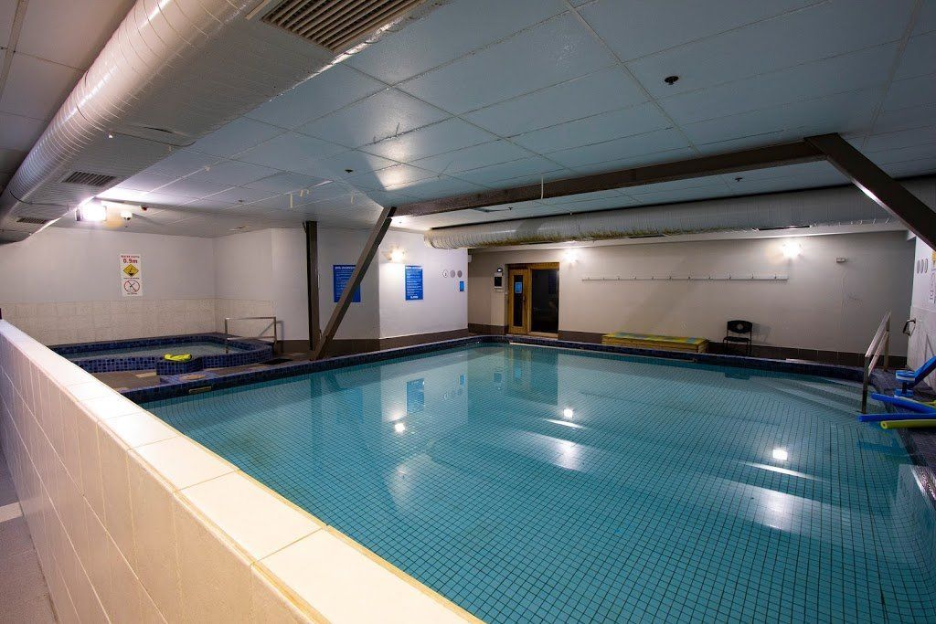Indoor swimming pool with blue water, tiled deck, and ceiling lights in a quiet recreation area