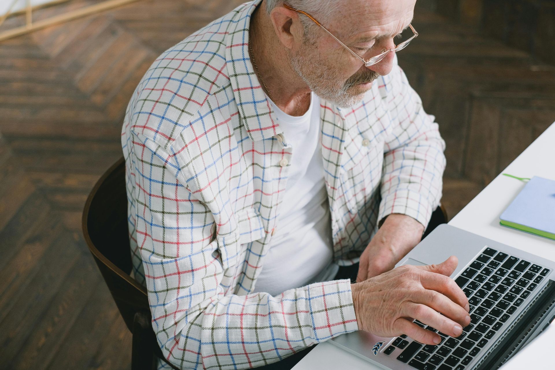 An older man is sitting at a desk using a laptop computer.