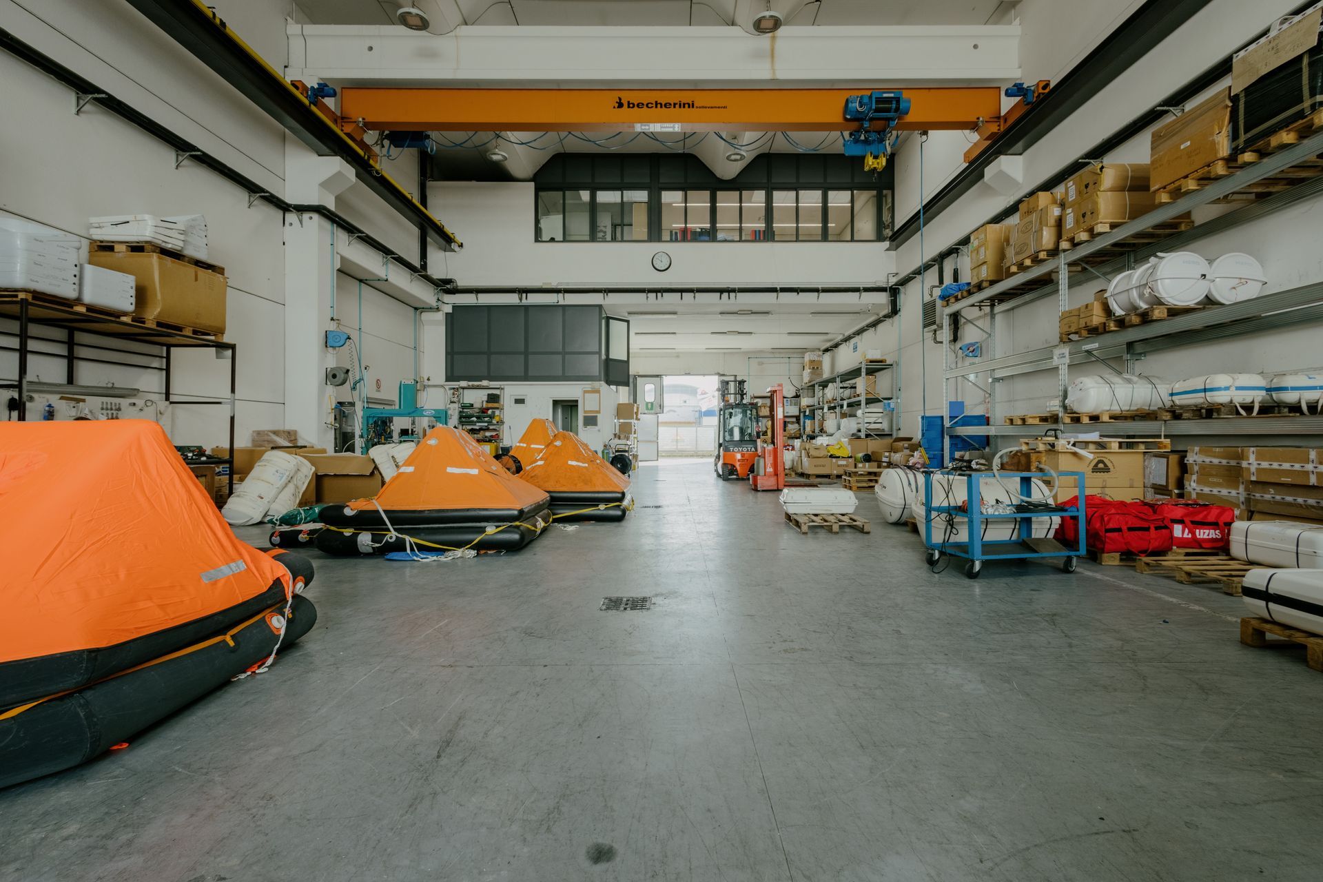 Wide industrial workshop with orange boats and equipment lined along both sides of a large open floor