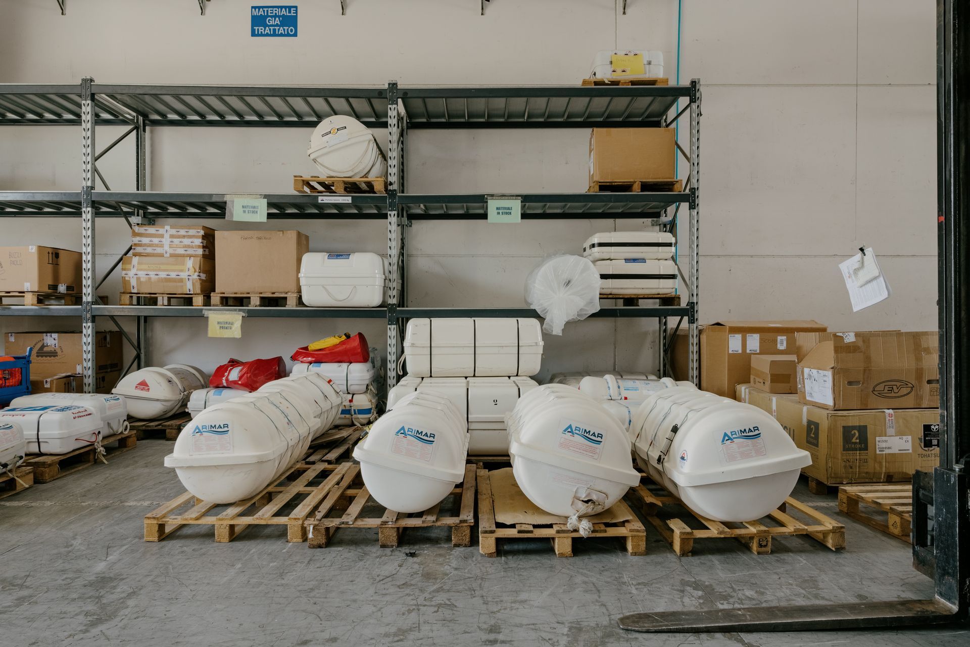 Warehouse storage shelves with stacked boxes, bags, and pallets in an industrial space.