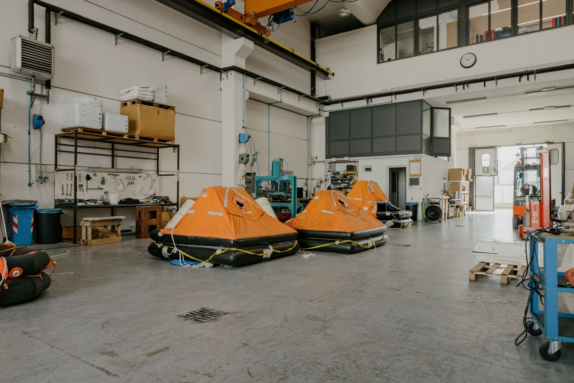 Orange rescue boats inside a bright industrial garage with tools and equipment along the walls