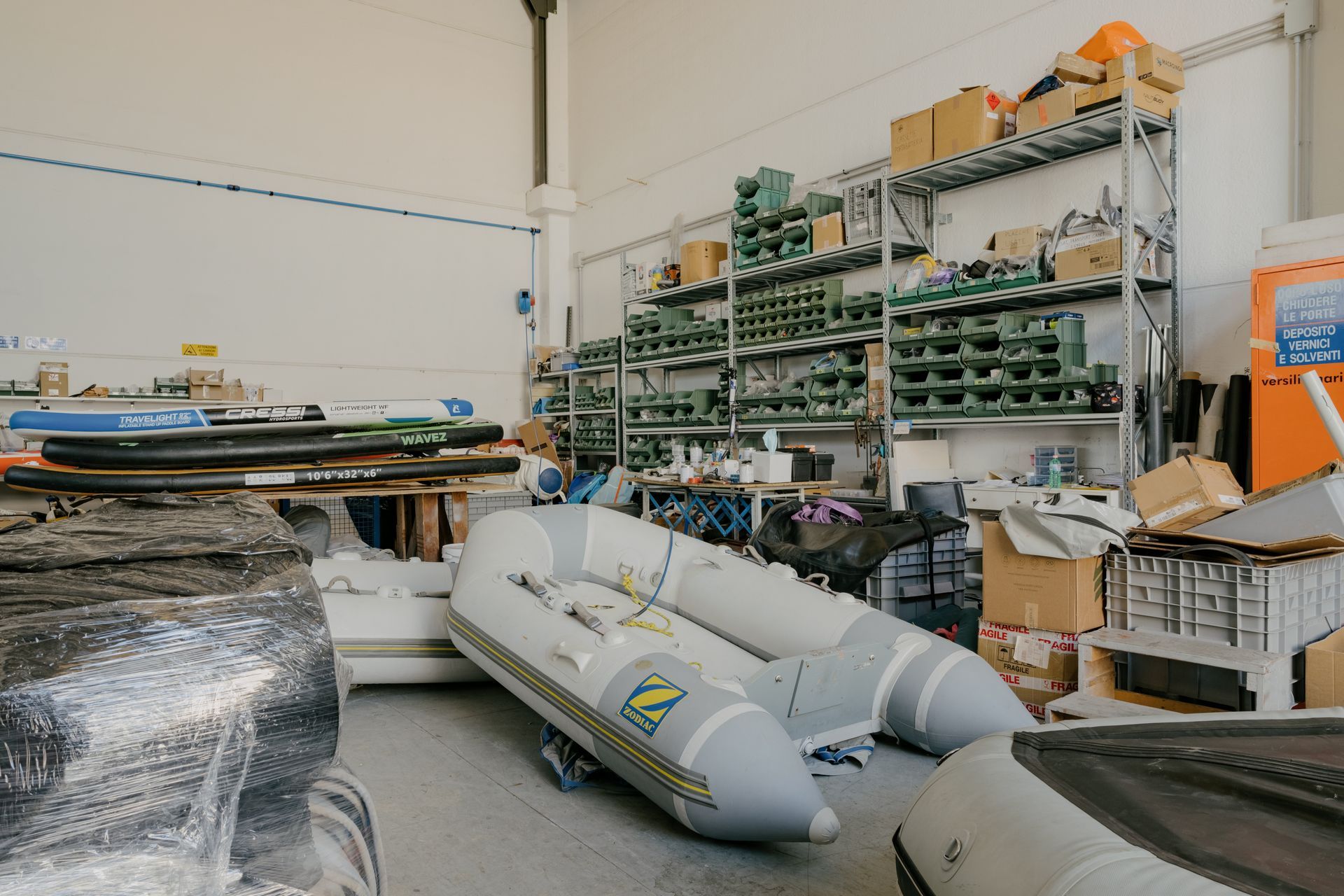 Workshop storage area with shelves, boxes, and a large gray inflatable boat on the floor.