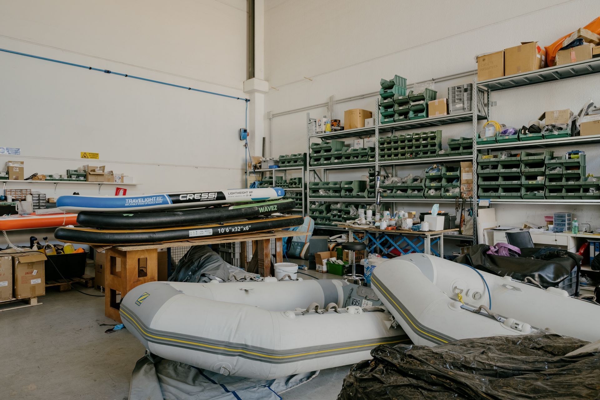 Workshop with stacked inflatable boats, shelves of supplies, and tools in a cluttered storage area.
